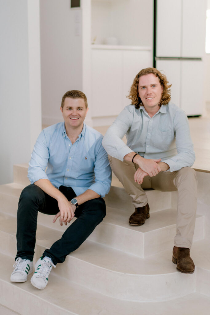 Coastal Letting Group Directors Chris de Closey and Luke Shore sitting on a staircase in a holiday home.