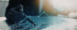 Close-up of a hand holding a pen over financial charts with a rising line graph, illustrating business growth, data analysis, and financial performance.